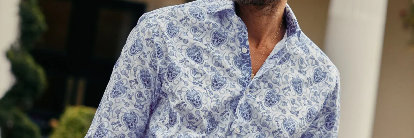 Close up of a man wearing a Blake Mill button up shirt. It's white with blue skull designs on it.